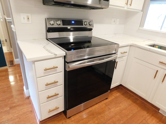kitchen featuring light stone counters, stainless steel electric range, light wood-style floors, and white cabinetry