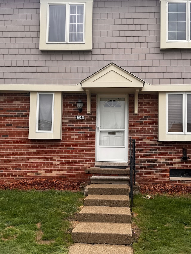 doorway to property featuring a yard and brick siding