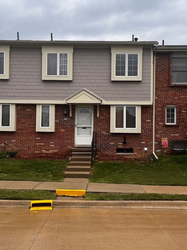 view of property with entry steps, a front lawn, and brick siding