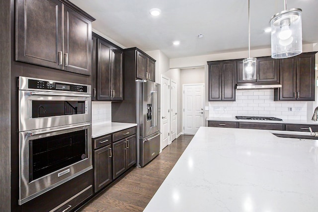 kitchen with dark brown cabinetry, backsplash, dark wood finished floors, a sink, and stainless steel appliances