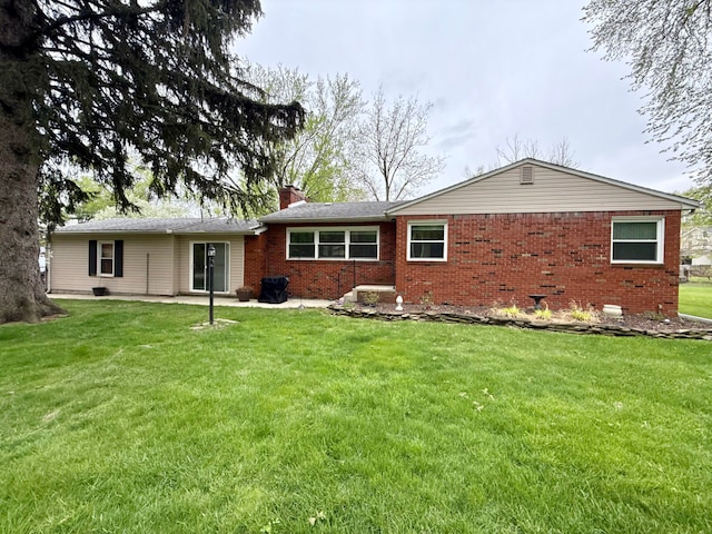 rear view of property with a chimney, a yard, a patio area, and brick siding
