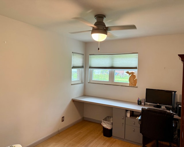 office area with built in study area, baseboards, ceiling fan, and light wood-style flooring