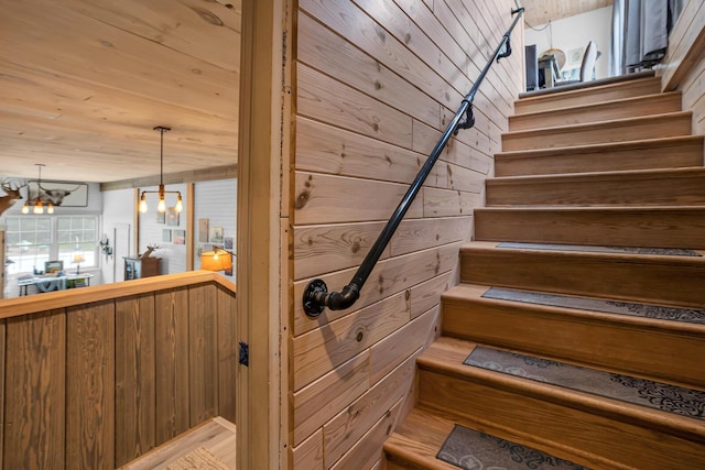 stairway with wood walls, a chandelier, and wooden ceiling