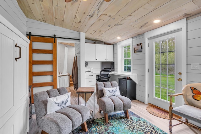 sitting room featuring wooden walls, a barn door, wood ceiling, and light wood-type flooring