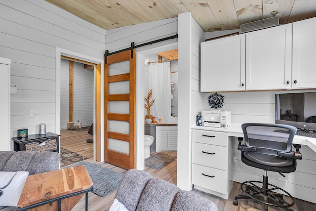 office area featuring light wood-style floors, built in study area, wooden walls, a barn door, and wood ceiling
