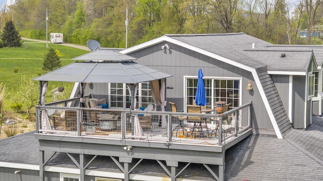 rear view of house with roof with shingles, outdoor dining space, a yard, and a deck