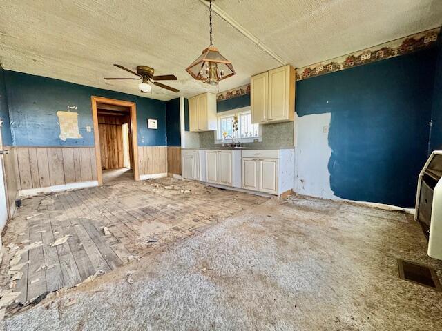 kitchen featuring a ceiling fan, a textured ceiling, wainscoting, and wooden walls