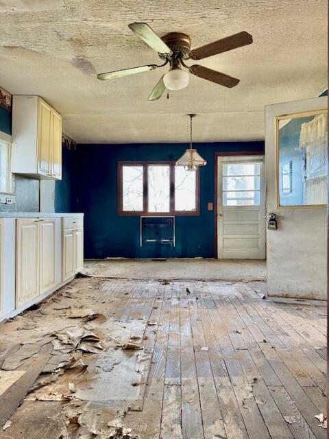 unfurnished dining area with light wood-type flooring, a ceiling fan, and a textured ceiling