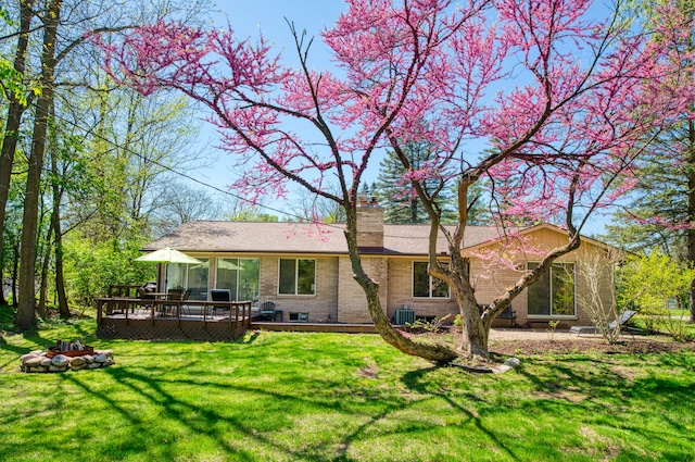 rear view of house featuring a fire pit, brick siding, a wooden deck, a lawn, and a chimney