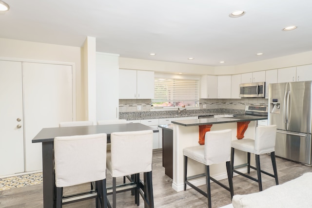 kitchen featuring appliances with stainless steel finishes, a kitchen island, a breakfast bar, white cabinets, and recessed lighting