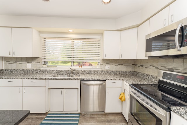 kitchen featuring stainless steel appliances, a sink, wood finished floors, white cabinets, and recessed lighting