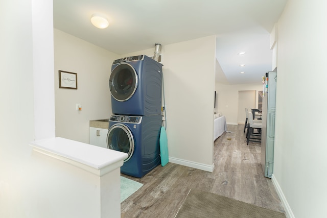 clothes washing area featuring stacked washer and clothes dryer, light wood finished floors, baseboards, and recessed lighting