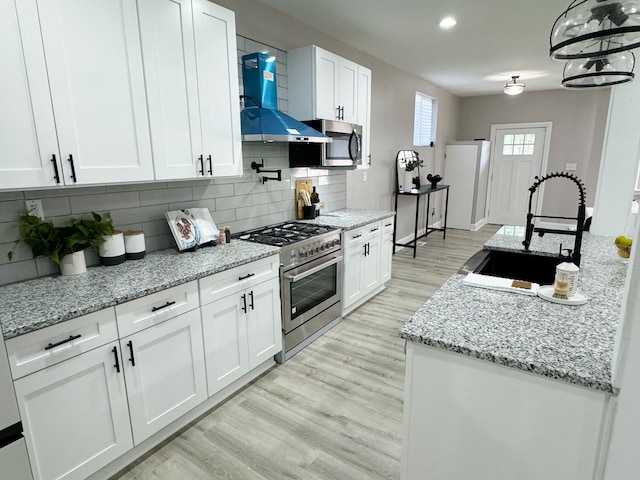 2439 Sheridan St, Detroit, MI 48214 - kitchen with wall chimney range hood, white cabinetry, a sink, stainless steel appliances, and light wood-style flooring