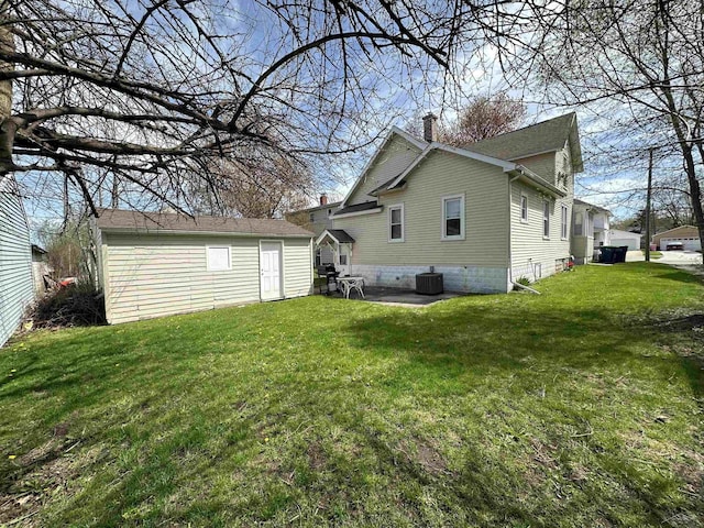 back of property with an outdoor structure, central AC unit, a chimney, and a yard