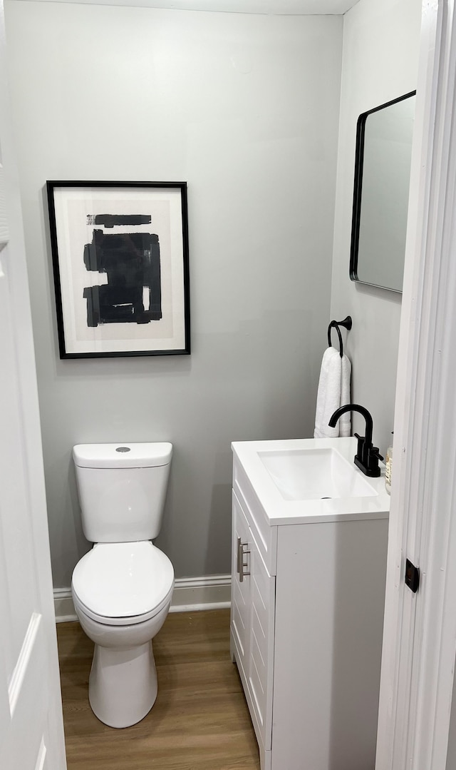 half bathroom with baseboards, wood finished floors, toilet, and vanity