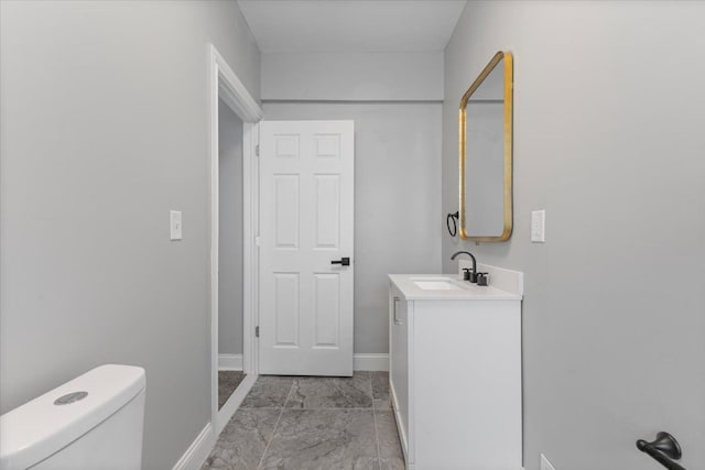 half bathroom featuring baseboards, marble finish floor, toilet, and vanity