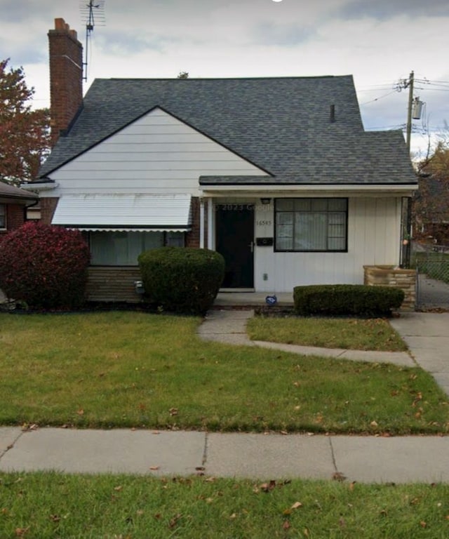 16545 E 8 Mile Rd, Eastpointe, MI 48021 - view of front of property featuring fence, a shingled roof, a front lawn, brick siding, and a chimney
