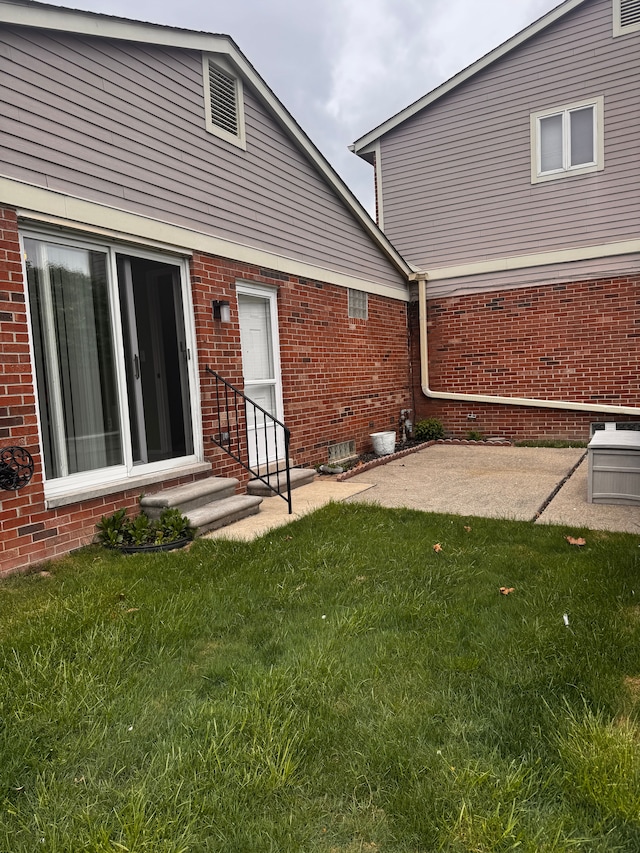 back of property featuring entry steps, a yard, a patio area, and brick siding