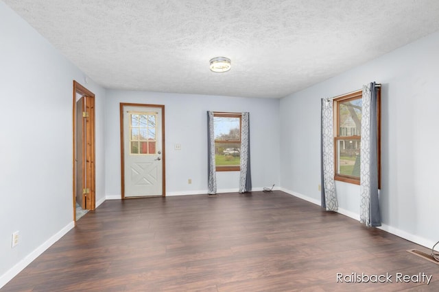 empty room with dark wood-style flooring, a textured ceiling, and baseboards