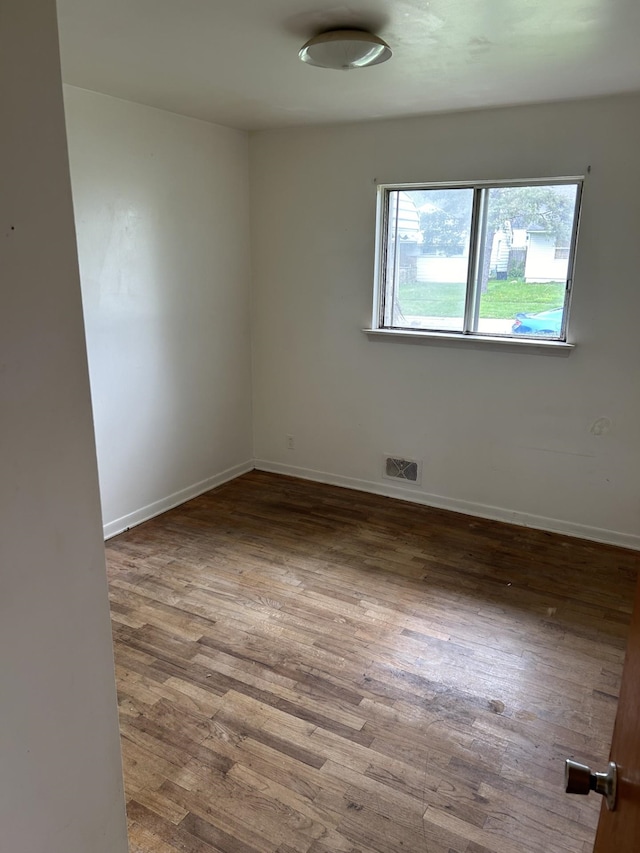 unfurnished room featuring baseboards, visible vents, and wood finished floors