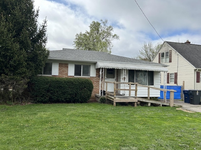 view of front of property featuring roof with shingles, a deck, a front lawn, and brick siding