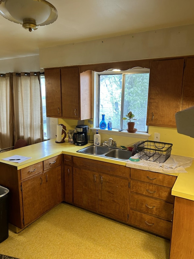 kitchen with a peninsula, light floors, light countertops, brown cabinets, and a sink