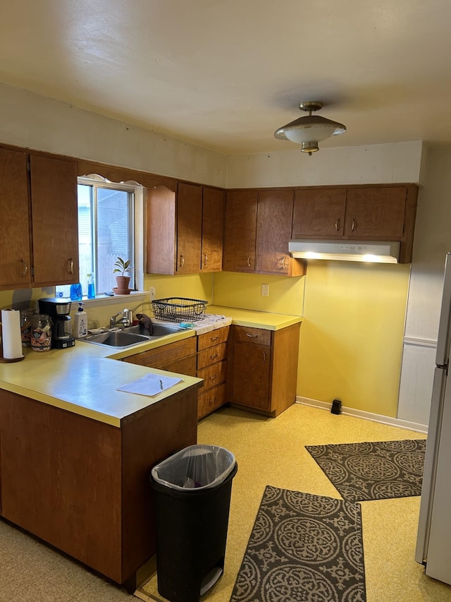 kitchen with a sink, light floors, under cabinet range hood, and light countertops