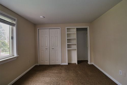 unfurnished bedroom featuring baseboards, multiple closets, and carpet