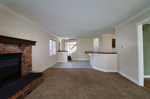 unfurnished living room with crown molding, carpet flooring, baseboards, and a brick fireplace