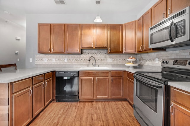 kitchen with stainless steel appliances, a sink, light wood-style flooring, a peninsula, and light countertops