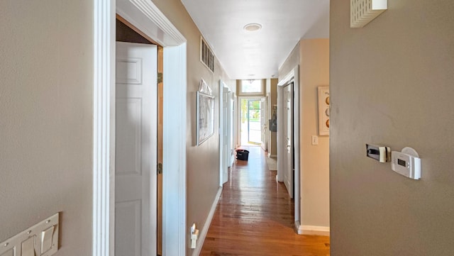 corridor with baseboards, wood finished floors, and visible vents