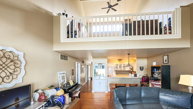 living room featuring visible vents, ceiling fan, a high ceiling, and wood finished floors