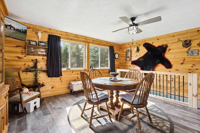 dining area with ceiling fan, wooden walls, and hardwood / wood-style floors