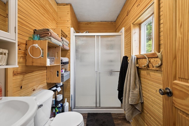 full bathroom with wood walls, toilet, a textured ceiling, a sink, and a stall shower