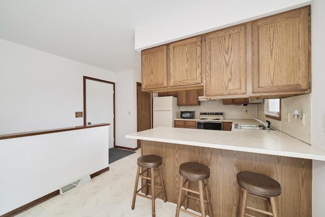 kitchen with a sink, white appliances, light countertops, a peninsula, and visible vents
