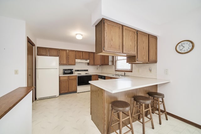 kitchen with brown cabinets, light countertops, a peninsula, under cabinet range hood, and white appliances