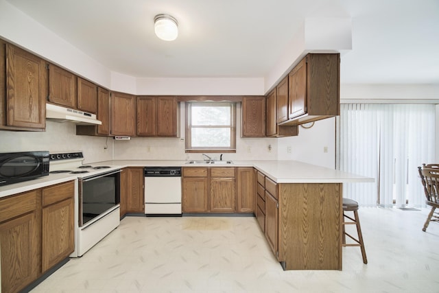 kitchen featuring a breakfast bar area, a sink, a peninsula, under cabinet range hood, and white appliances