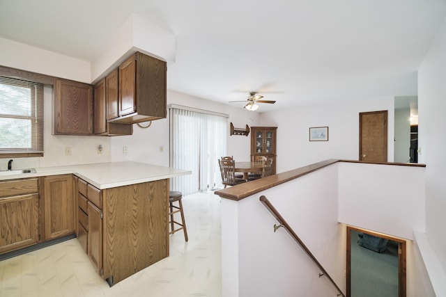 kitchen featuring a sink, a peninsula, light floors, a kitchen breakfast bar, and a ceiling fan