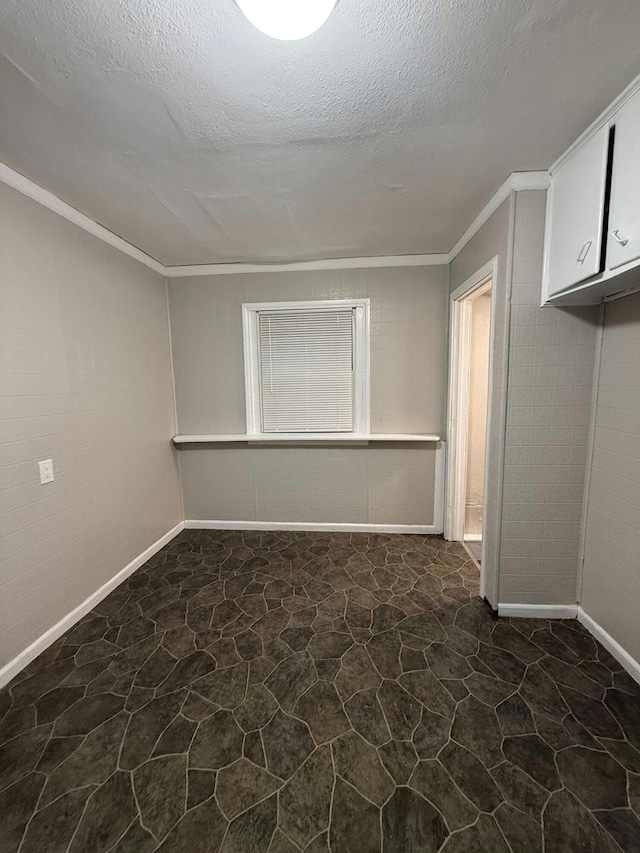unfurnished room featuring baseboards, a textured ceiling, crown molding, and stone floors