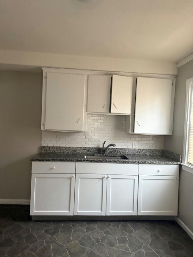kitchen featuring dark tile patterned floors, decorative backsplash, a sink, baseboards, and white cabinets