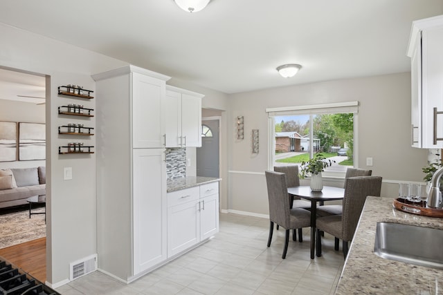 kitchen featuring light stone countertops, visible vents, a sink, white cabinetry, and decorative backsplash