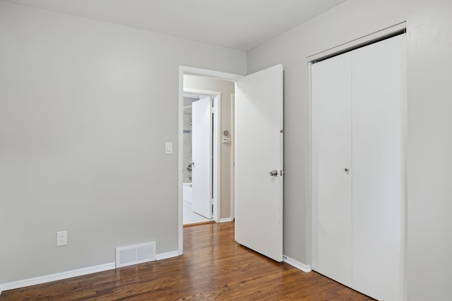 unfurnished bedroom with a closet, visible vents, wood finished floors, and baseboards