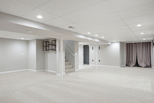finished below grade area featuring stairs, a drop ceiling, light carpet, and visible vents
