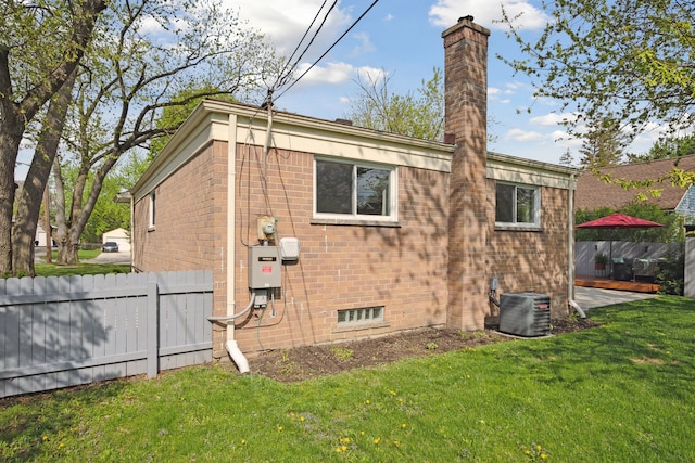 view of side of property with central air condition unit, fence, brick siding, a chimney, and a lawn