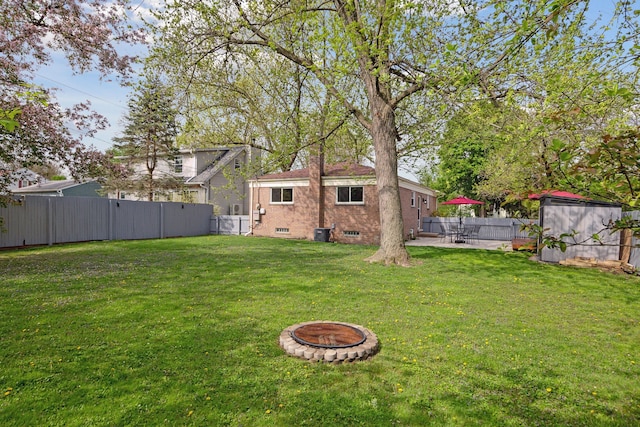 view of yard featuring a storage shed, a patio, an outdoor fire pit, a fenced backyard, and an outbuilding