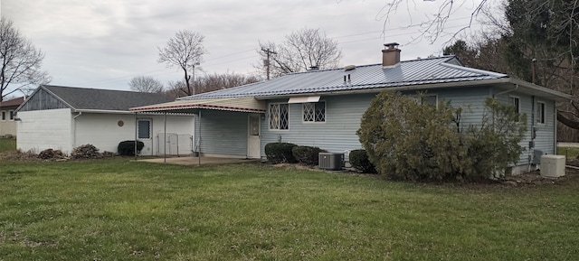 back of house featuring a chimney, cooling unit, a yard, metal roof, and a patio