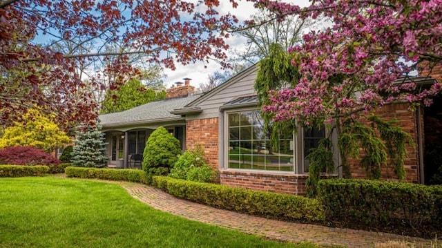 view of property exterior with a chimney, a yard, and brick siding
