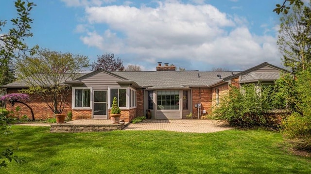 rear view of house with a patio, a chimney, brick siding, and a lawn