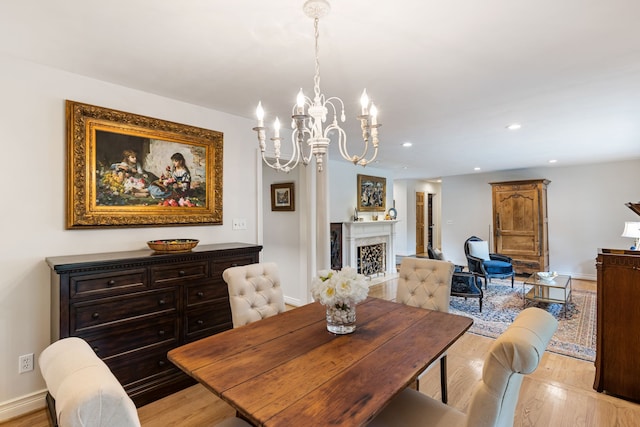 dining area featuring baseboards, light wood-style flooring, a fireplace, and a notable chandelier