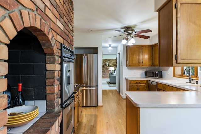 kitchen with appliances with stainless steel finishes, a sink, a peninsula, light countertops, and light wood-type flooring